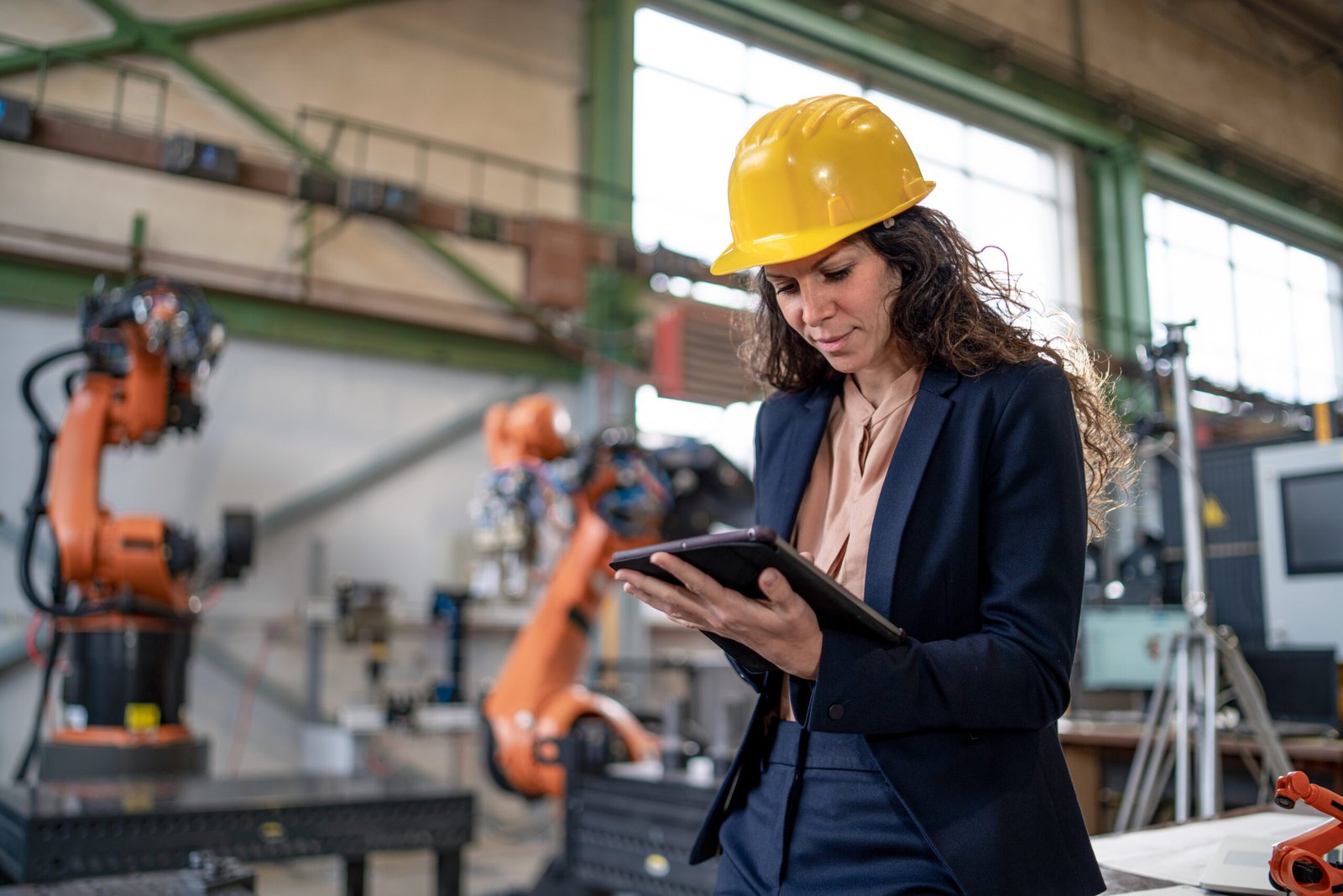 Automation female engineer with tablet for programming robotic arm in factory.