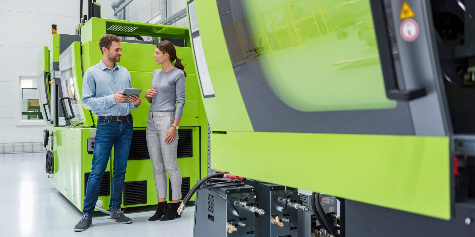 Colleagues in high tech company controlling manufacturing machines, using digital tablet